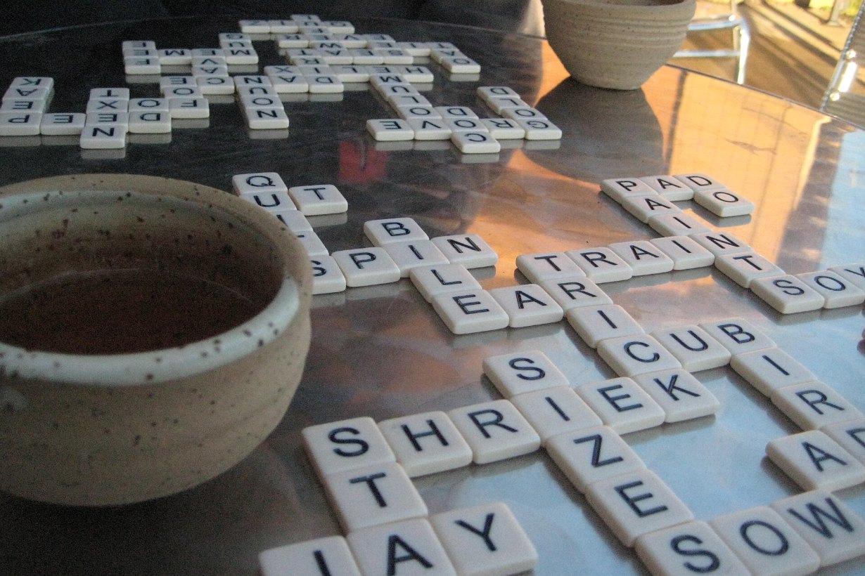 Bokstavsbrickor från ordspelet Bananagrams utlagda på ett bord bredvid en tekopp